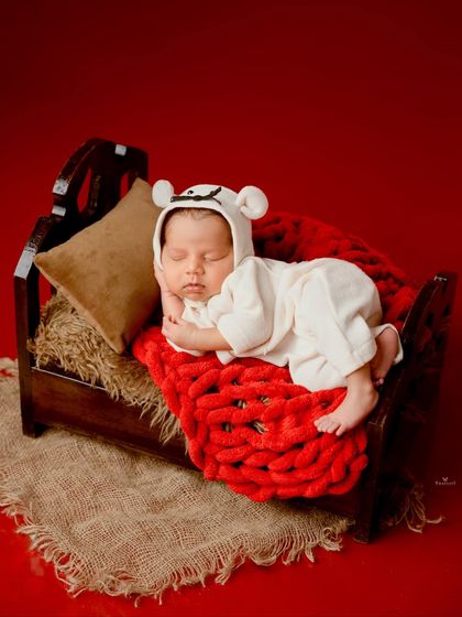 A close-up portrait of the newborn sleeping on the tiny bed, highlighting the adorable bear hat and the cozy textures.
