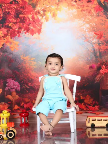 A baby boy sits on a white chair in the middle of an enchanted autumn forest. The rich colors and soft lighting make this a stunning and artistic portrait.