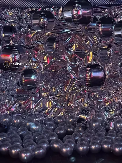 A unique and futuristic photobooth with a crumpled silver foil backdrop and metallic orbs.