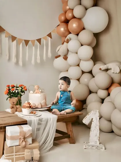 A classic first birthday studio portrait. The neutral tones of the balloons and props keep the focus on the birthday boy and the big number one.