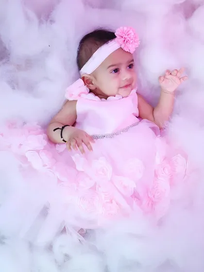 An ethereal, dreamy shot of the baby girl lying back in the pink-lit clouds.