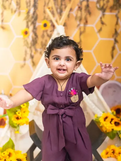 An energetic shot of a baby girl with her arms out, enjoying her sunflower-themed studio session.
