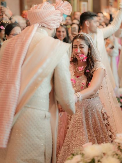 A candid moment of pure joy as the bride laughs with flower petals on her face during the Varmala ceremony.