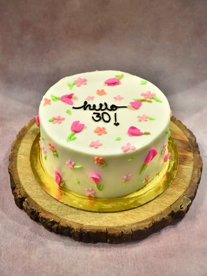 "Hello 30!" A sweet and simple cake to mark a milestone birthday, decorated with delicate, hand-piped pink and peach flowers on a smooth white buttercream base.