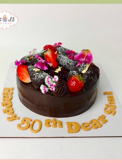 A decadent chocolate cake celebrating a 50th birthday. It's topped with fresh strawberries, edible flowers, and a touch of gold leaf for a luxurious finish.