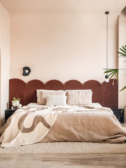 A view of the bedroom through its defining arches. The scalloped, burnt cinnamon headboard adds a touch of warmth and playful geometry against the soft beige walls.
