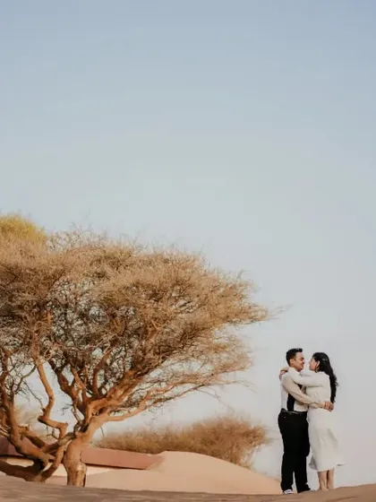 A beautiful wide shot of a couple embracing under a lone tree in the vast Abu Dhabi desert. This image has a powerful, iconic feel, symbolizing their connection in the midst of a grand landscape.