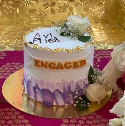 An elegant engagement cake with a purple watercolor effect and gold leaf accents. The cake is set on a beautiful brocade fabric, perfect for a traditional ceremony.