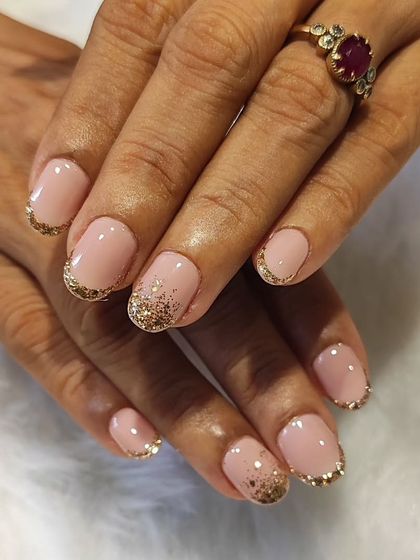 A touch of gold for a luxurious feel. This is a beautiful French manicure on short, rounded nails with sparkling gold glitter accenting the tips.