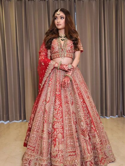A full-length shot of a guest in a stunning red lehenga. The makeup is glamorous and classic, perfect for a wedding.
