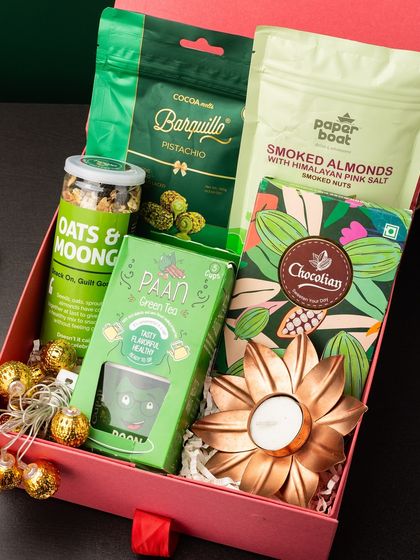 A duplicate of ID 25, this hamper is packed with healthy green-themed treats. It includes pistachio barquillo, smoked almonds, oats and moong, paan green tea, and a copper flower diya.