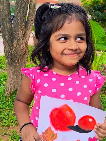 A young artist proudly holds her colorful still life painting of red fruits and autumn leaves.
