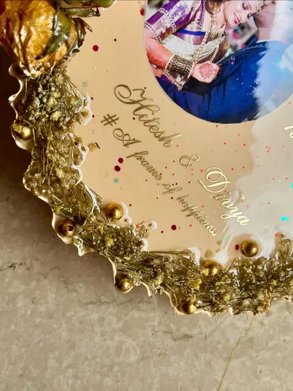 A close-up of an elegant flower photo frame. This custom frame showcases wedding flowers around a beautiful photo, with the couple's names and hashtag in golden perfection.