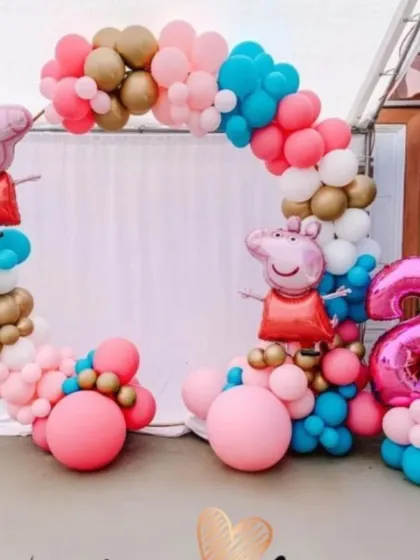 A playful Peppa Pig theme for a second birthday. This outdoor setup includes a circular balloon arch with Peppa Pig foil balloons, a large number '2' foil balloon, and a bright pink, blue, and gold color scheme.