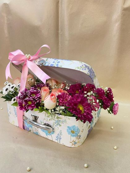 A vintage-style floral suitcase makes for a whimsical and romantic gift. This one is overflowing with a mix of roses and chrysanthemums, tied with a simple pink ribbon.