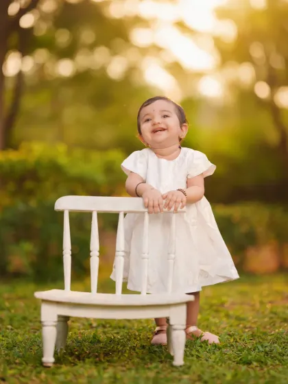 A sweet and simple outdoor portrait taken during the golden hour. The soft, warm light beautifully highlights this little girl's happy expression as she stands by a small white chair.
