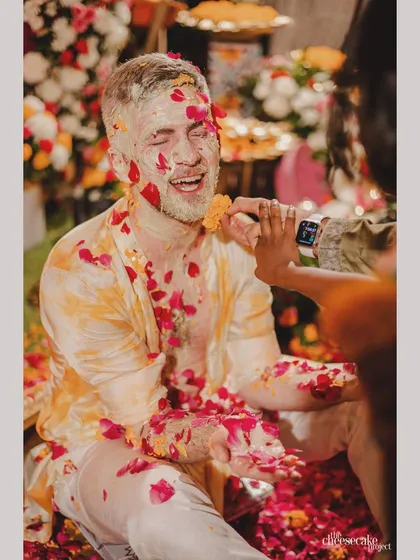 The groom enjoying the playful traditions of the Haldi ceremony, surrounded by a shower of red and yellow flower petals.