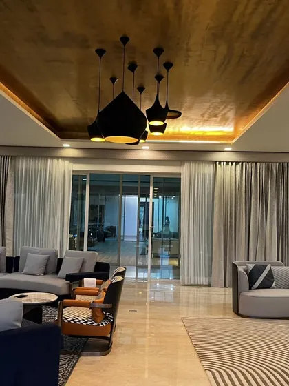 The living room at our Vasant Kunj farmhouse project features a dramatic gold-textured ceiling and modern black pendant lights. The design combines sleek, contemporary furniture with bold patterns, creating a sophisticated and inviting atmosphere for a large family.