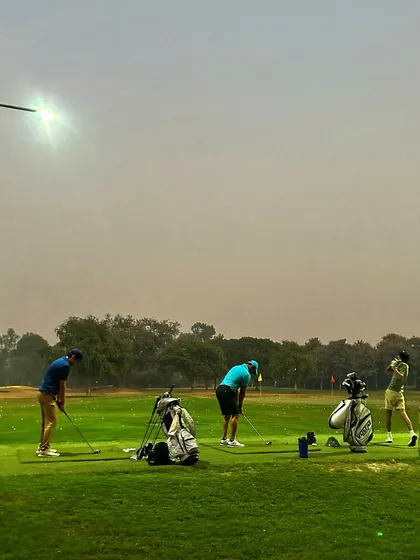 A group of golfers practices under the lights, enjoying a cool evening session on the range.