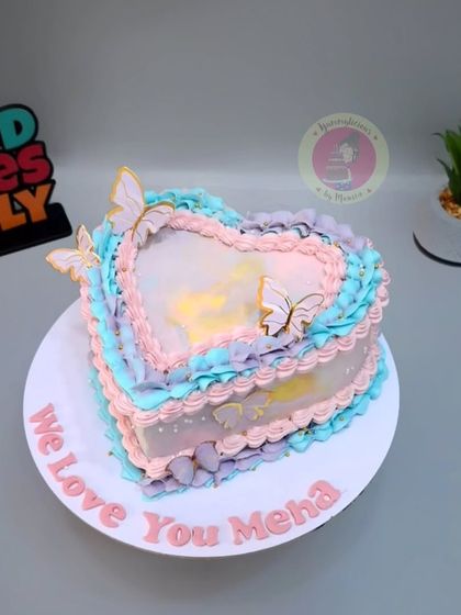 A heart-shaped vintage cake in pastel shades of pink, blue, and purple, decorated with delicate piping and butterflies.