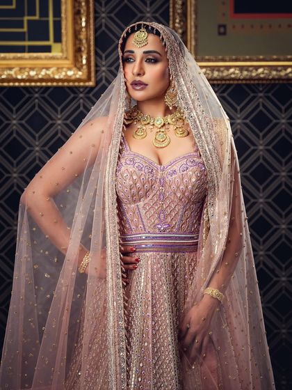 A regal bridal portrait featuring a heavily embroidered lehenga and a sheer veil. The lighting and pose are designed to convey a sense of majesty and grace, suitable for high-end bridal campaigns.