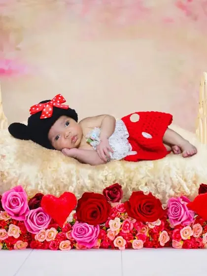 An adorable Minnie Mouse themed newborn shoot, with the baby in costume on a bed of red roses.