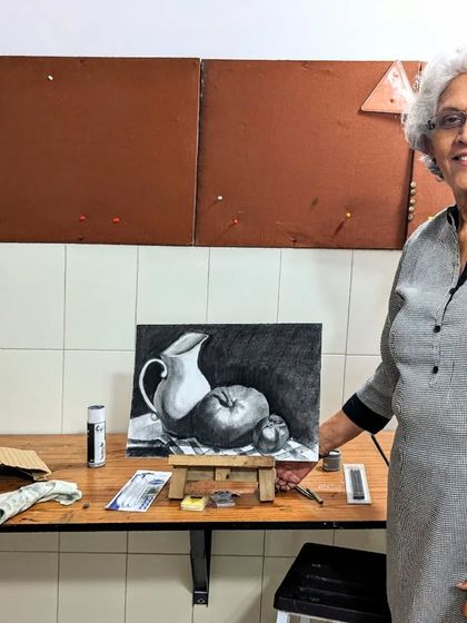 It's never too late to pursue a passion for art. One of our adult students from a hobby class proudly stands with her completed charcoal still life, a testament to her dedication and progress.
