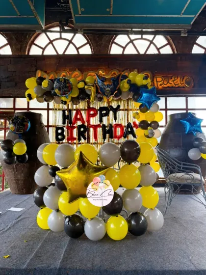 A Batman-themed birthday decoration with a yellow and black balloon wall and 'Happy Birthday' foil letters.