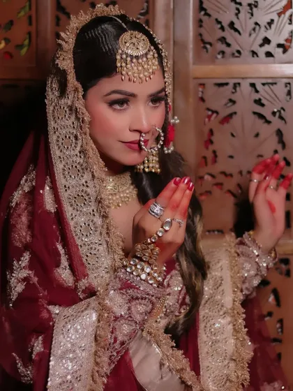 This shot captures the grace of the model's hand gestures, adorned with henna, against her rich maroon outfit.