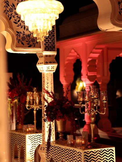 A view through the architectural pillars, showing consoles styled with candelabras and floral arrangements. The chevron-patterned tables with thikri work add another layer of traditional Rajasthani craft.