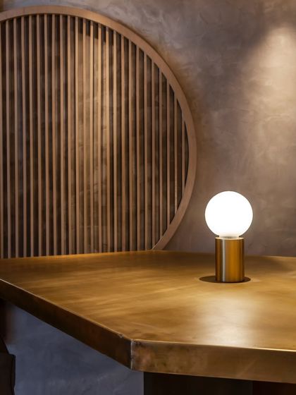 A minimalist lamp casts a soft glow on a brass-topped table, highlighting the clean lines and modern aesthetic of our design.