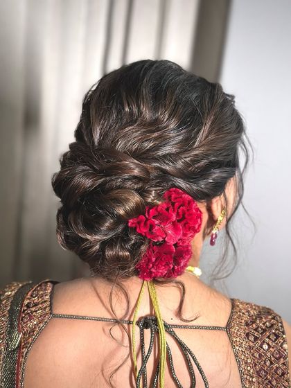 A textured low bun decorated with red carnations, perfect for adding a pop of color to your look. This style is ideal for a festive occasion or a wedding party.