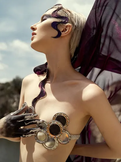 The sunlight catches the shimmer in the dark eyeshadow and the gloss on the sculpted hair, adding dimension to the 'Siren' look.