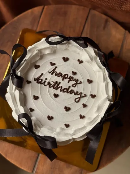 A Pinterest-inspired birthday cake with a clean white finish, delicate chocolate hearts, and chic black ribbon bows.