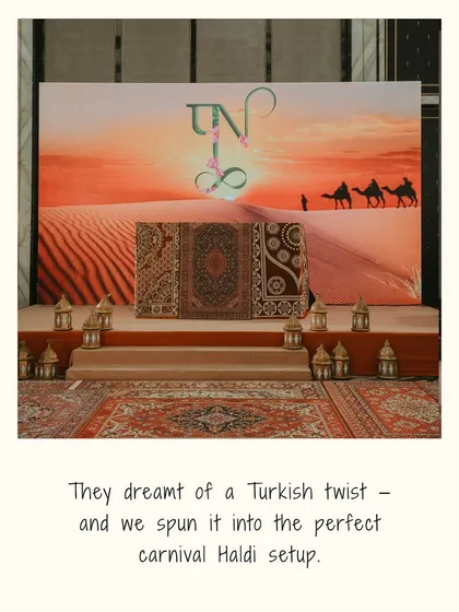 A photo backdrop for the Turkish Haldi, featuring a desert sunset scene, Persian rugs, and traditional lanterns, perfectly executing the couple's vision.