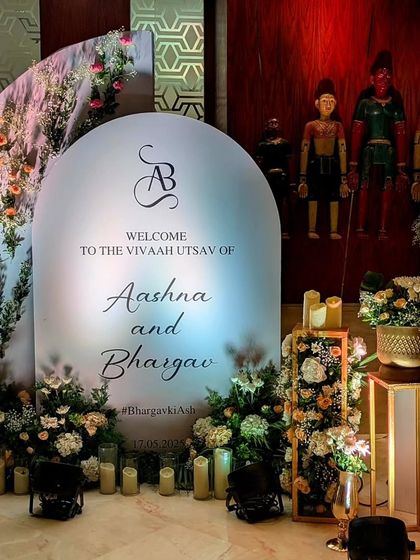 A modern arched welcome sign for Aashna and Bhargav, featuring their custom monogram. The sign is surrounded by soft florals and candlelight, creating a romantic and personalized entryway.