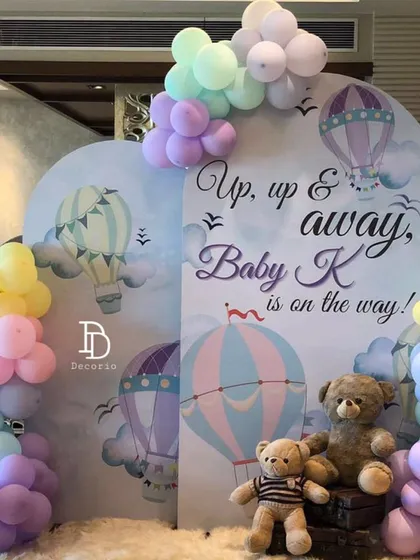 The "Up, up & away, Baby K is on the way!" theme is perfect for a whimsical baby shower. This setup features hot air balloon illustrations on the backdrops and soft, pastel-colored balloon clusters that look like clouds.