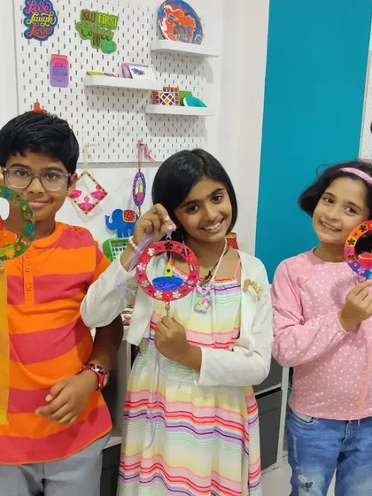 Three happy kids proudly showing off the colorful Diwali diya hangings they created at a birthday party.