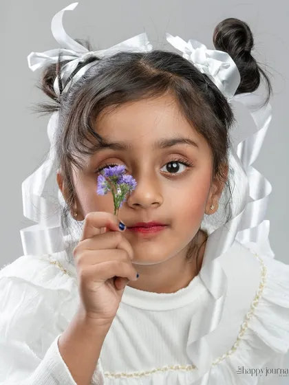 Capturing the innocence and wonder of childhood in a creative portrait. This studio shot for a child's portfolio uses soft lighting and simple props like the flower and ribbons to create a sweet, artistic image that feels both timeless and full of personality.