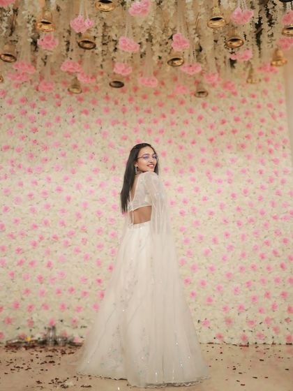This stunning white lehenga with cape-like sleeves creates a dramatic and glamorous silhouette against a floral backdrop. It's an ideal rental for making a grand entrance.