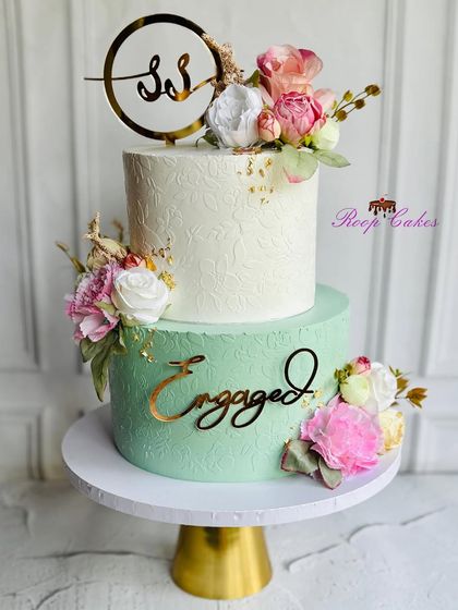 A lovely two-tier engagement cake in a refreshing mint green and white. The design is enhanced with a delicate stencil pattern, fresh flowers, and the couple's initials for a personal touch.