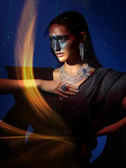 A shot from a cosmic-themed jewelry campaign, where the styling is designed to evoke the feeling of a supernova. The look combines a structured black gown with dramatic, celestial-inspired makeup and layers of statement diamond jewelry.