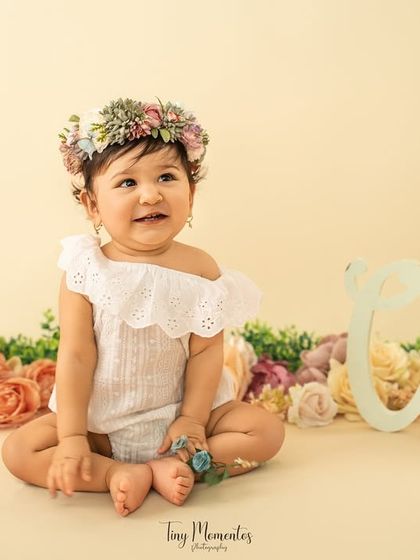 A sweet, gentle smile from the birthday girl, surrounded by a garden of soft pastel flowers for her one-year milestone shoot.