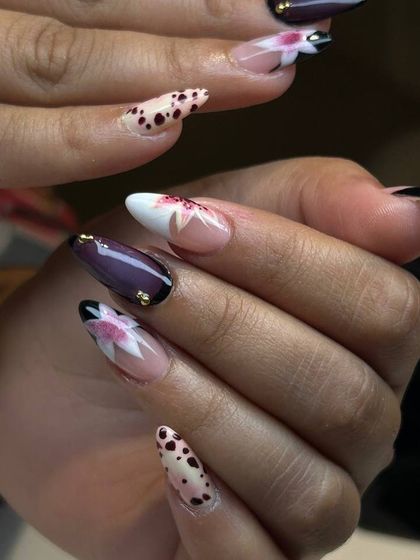 A unique and artistic nail design. This set features a mix of patterns, including dalmatian spots and abstract florals, with delicate gold stud accents.
