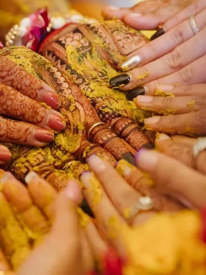 A close-up shot of hands with intricate henna designs being coated in turmeric, capturing the textures and colors of the tradition.