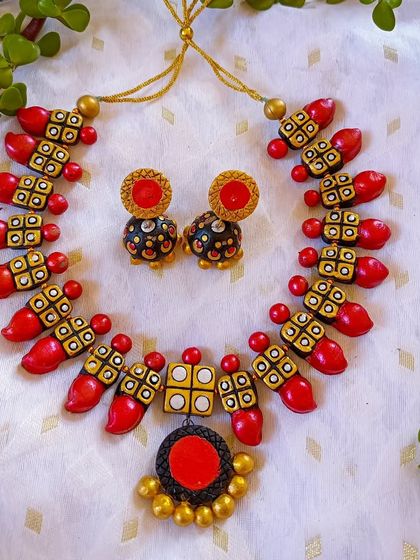 A beautiful terracotta necklace in red and yellow, with a unique pendant design. It's perfect for pairing with a silk saree to be the diva of any event.
