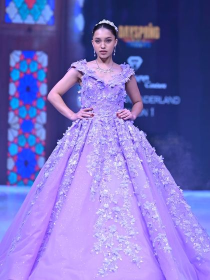 A vision in lavender. This regal ball gown features a cascade of 3D floral appliqués over a glittering tulle skirt, designed to make you feel like you are walking through a field of flowers.