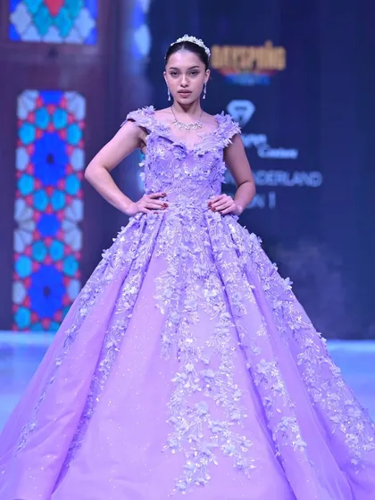 A vision in lavender. This regal ball gown features a cascade of 3D floral appliqués over a glittering tulle skirt, designed to make you feel like you are walking through a field of flowers.