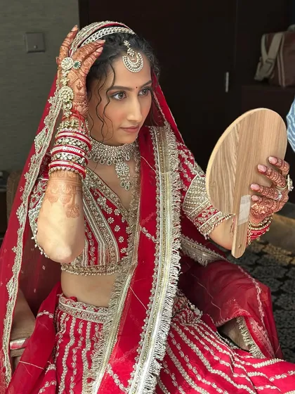 The final check in the mirror. This bride is adjusting her dupatta, giving a glimpse of her intricate red and silver lehenga and the soft, glowing makeup that completes her D-day look.