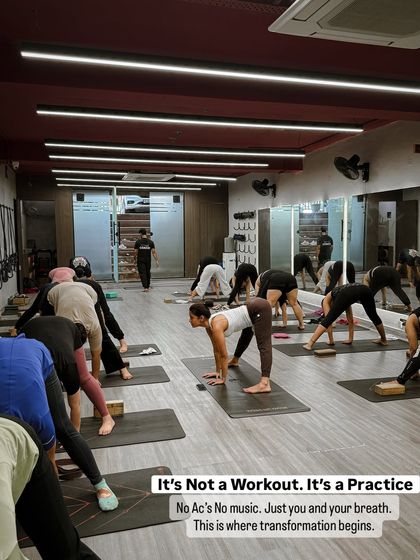 A class moving through a forward fold sequence in our Ashtanga practice. The text overlay reminds us that this is a practice, not a workout, built on the foundation of just you and your breath.